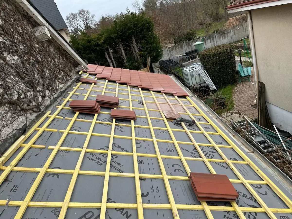 Chantier de réfection vu de haut : écran de sous-toiture gris posé, liteaunage neuf et premières tuiles plates en tête de pan